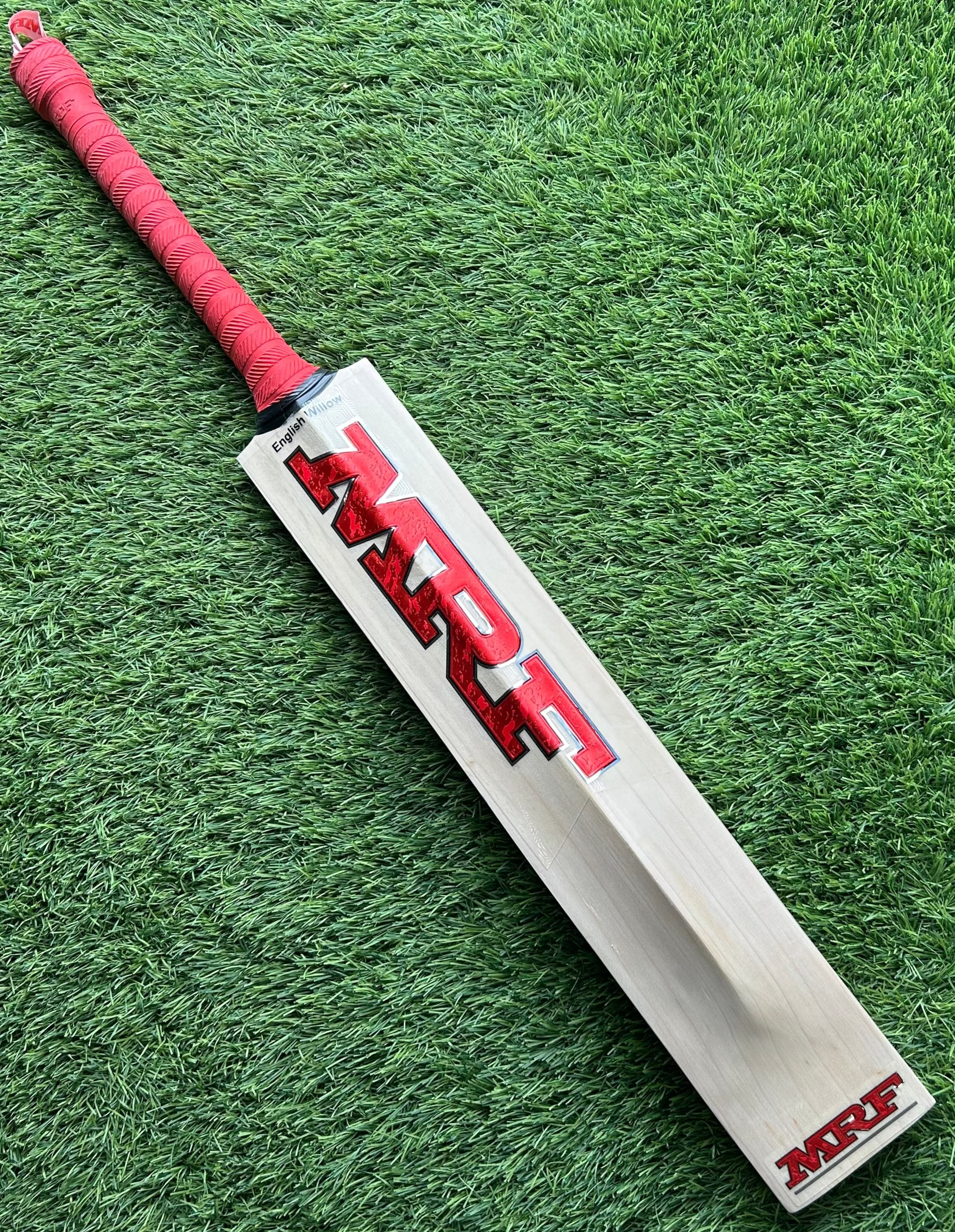 White cricket bat with red lettering on a green grass background
