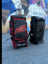 Two AKS CRICKET Legend Pro wheeled cricket kit bags in black and red, featuring durable fabric and multiple pockets.